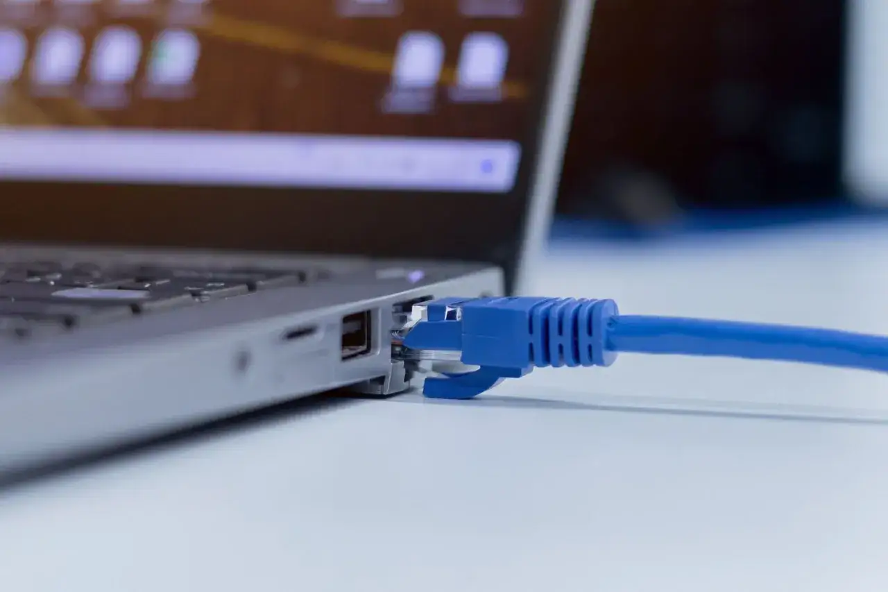 Niebieski kabel sieciowy podłączony do portu Ethernet laptopa. Prosty sposób, jak podłączyć kabel sieciowy do komputera.