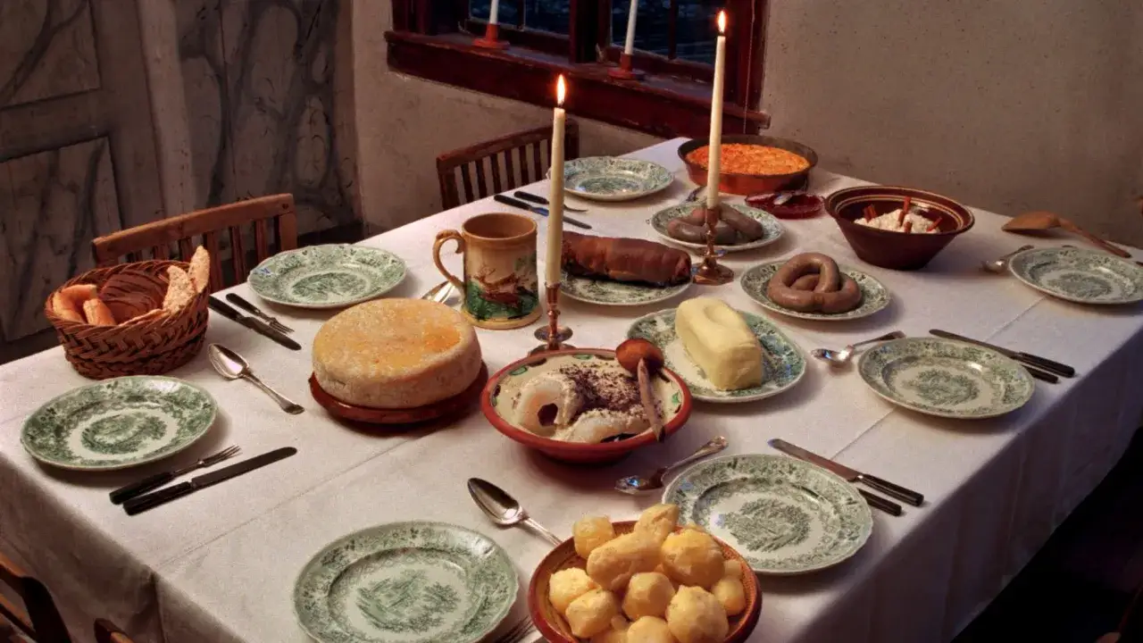 En dukad festmåltid med lutfisk, korv, ost, bröd och potatis. Tända ljus skapar stämning, perfekt för att njuta av vin till lutfisk.