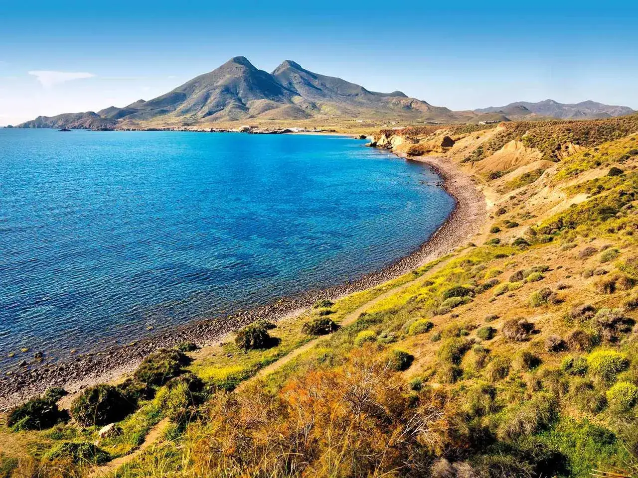 Costa salvaje de **Cabo de Gata** con mar azul turquesa, montañas al fondo y vegetación árida en las laderas.