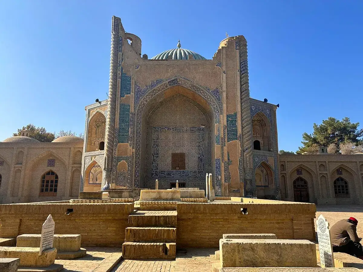 Pr&auml;chtige Moschee mit blauen Kacheln in Balkh, Afghanistan. Ein Mann sitzt im Schatten und liest.