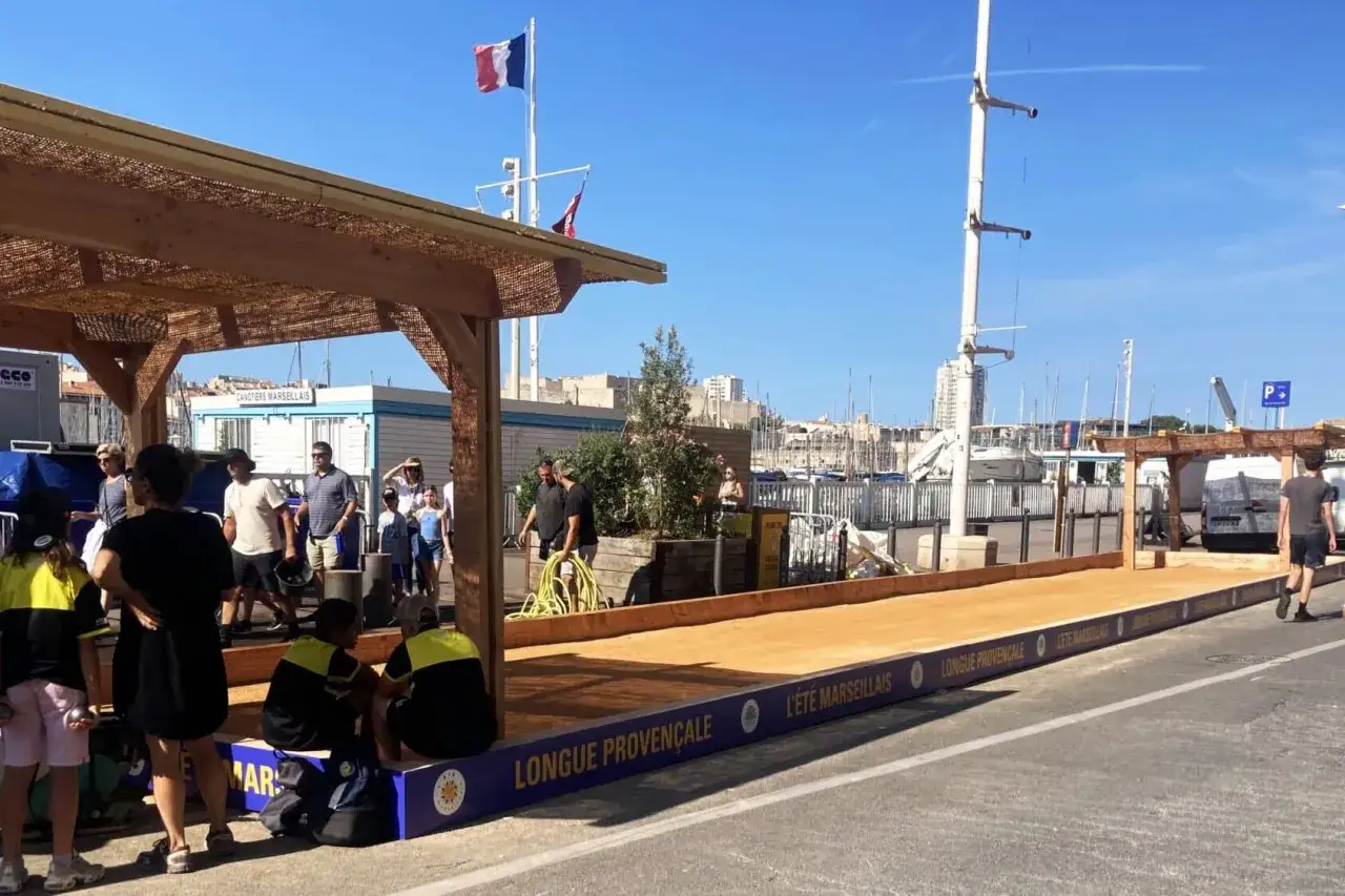 Des joueurs de boules profitent d'un &eacute;t&eacute; marseillais ensoleill&eacute; sur un terrain de jeu en bord de mer.