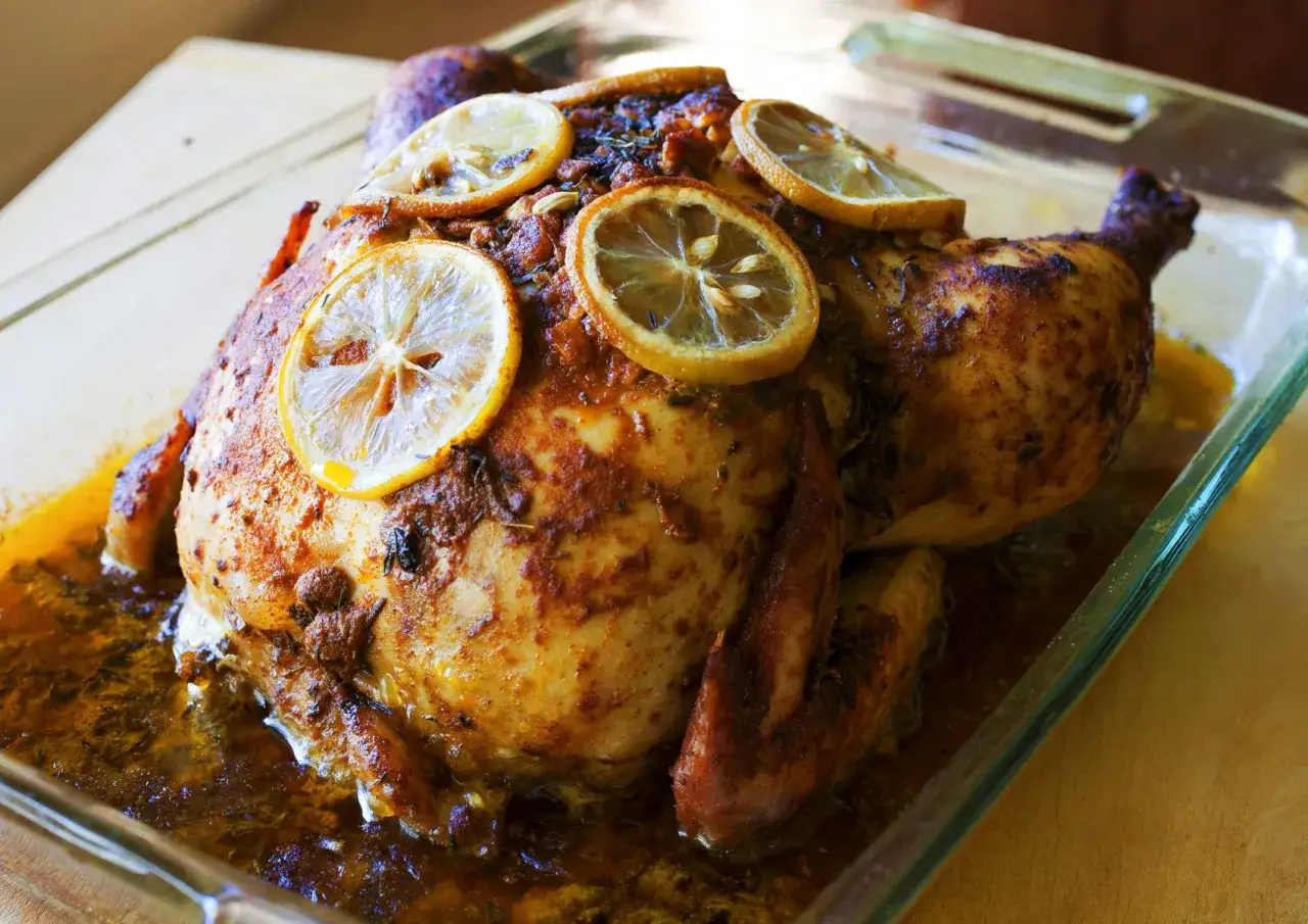 Pollo entero asado con especias cajun y rodajas de limón, jugoso y dorado en una bandeja de vidrio.