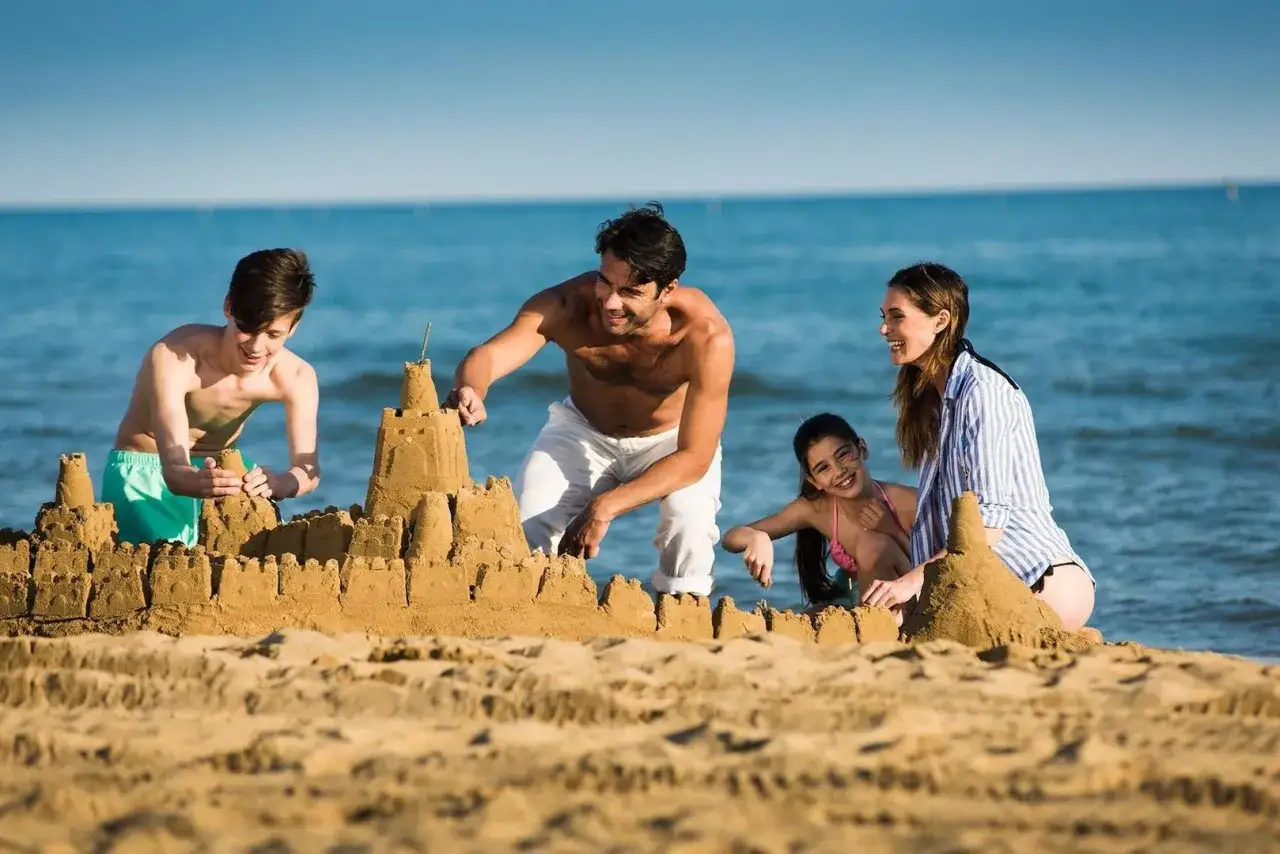 Famiglia felice costruisce un castello di sabbia, un'idea perfetta per sapere dove andare in vacanza con i bambini all'estero.