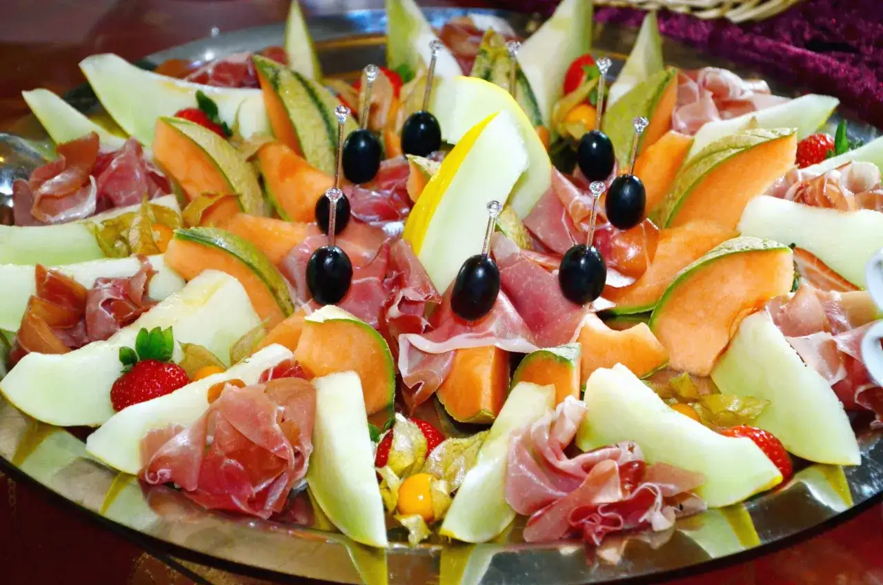 Plateau de melon et jambon cru, une pr&eacute;sentation originale avec des olives noires sur des pics d&eacute;coratifs.