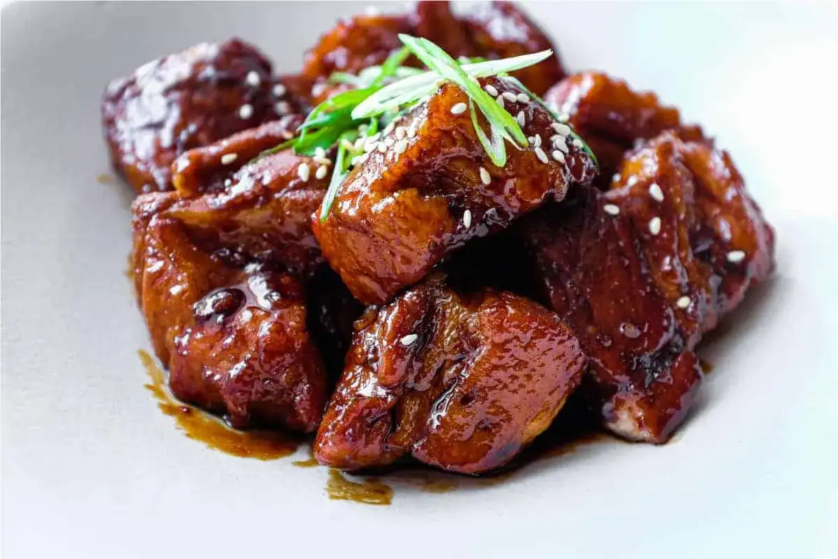 A pile of glistening, glazed japanese pork belly pieces, sprinkled with sesame seeds and garnished with fresh green onions.
