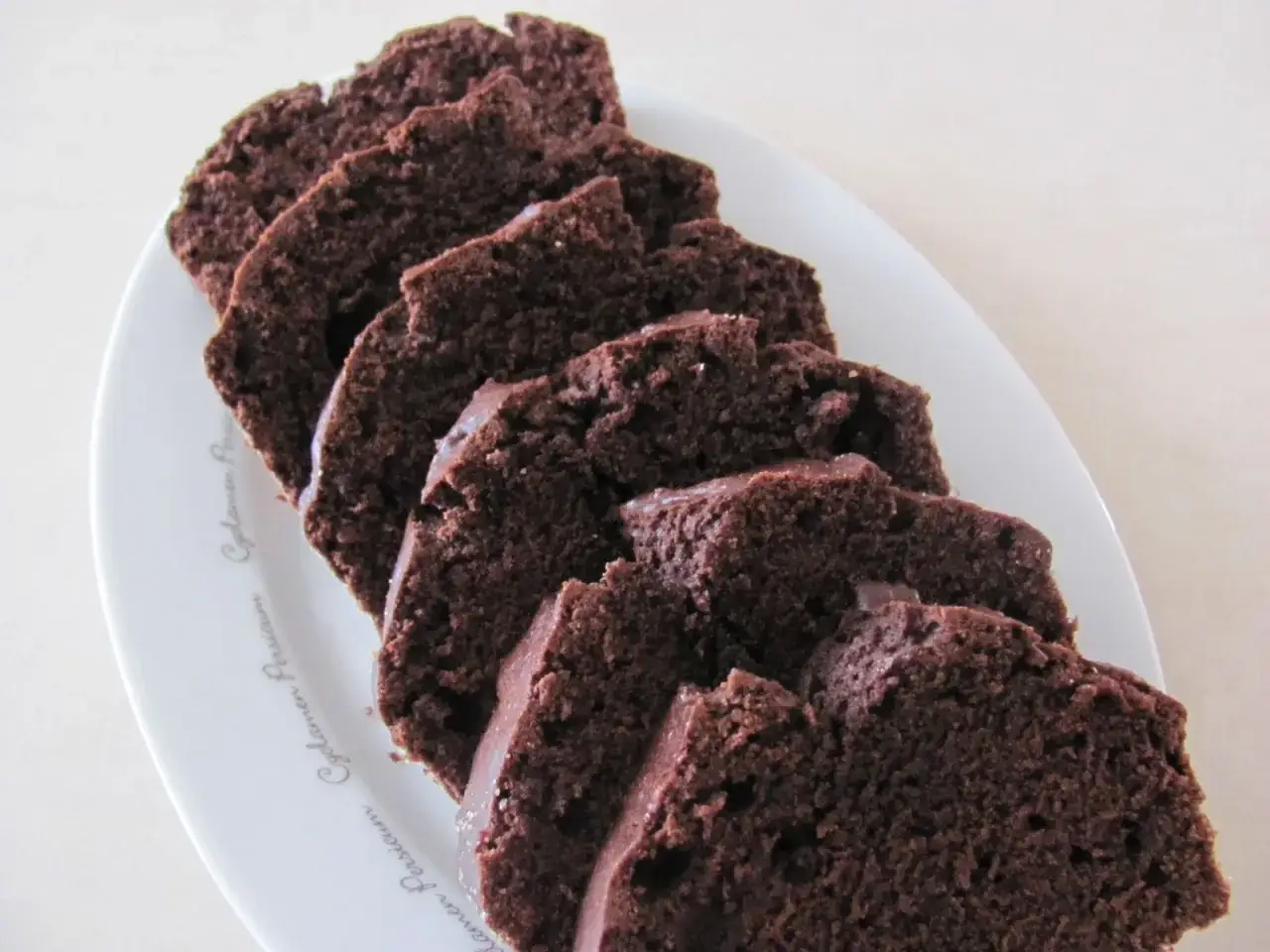 Pokrojona babka kakaowa ułożona na białym talerzu. Wilgotne ciasto z czekoladą kusi swoim aromatem.