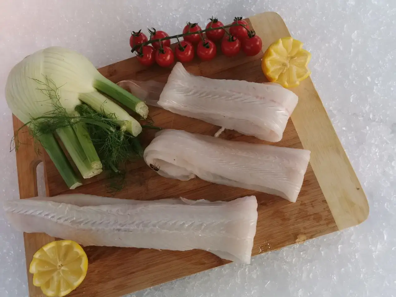 Trois filets de poisson sabre frais, prêts à être cuisinés avec du fenouil, des tomates cerises et du citron.
