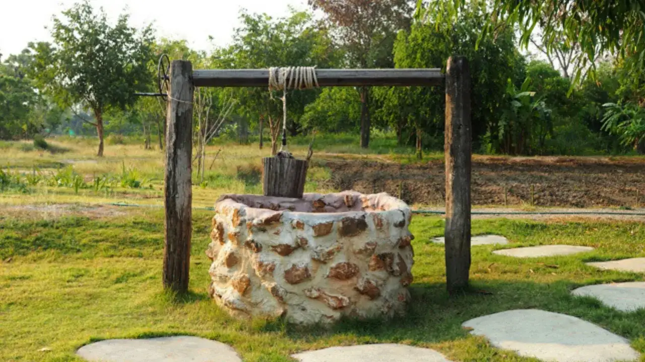Pozo de piedra con cubo de madera colgando. Interesado en cuanto cuesta hacer un pozo as&iacute; para tu jard&iacute;n.