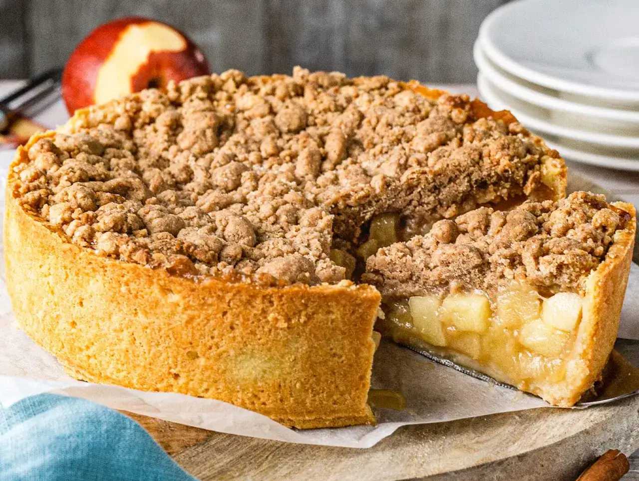 Saftiger veganer Apfelkuchen mit knuspriger Streuseldecke. Ein St&uuml;ck wurde bereits entnommen und zeigt die F&uuml;llung aus Apfelst&uuml;cken.