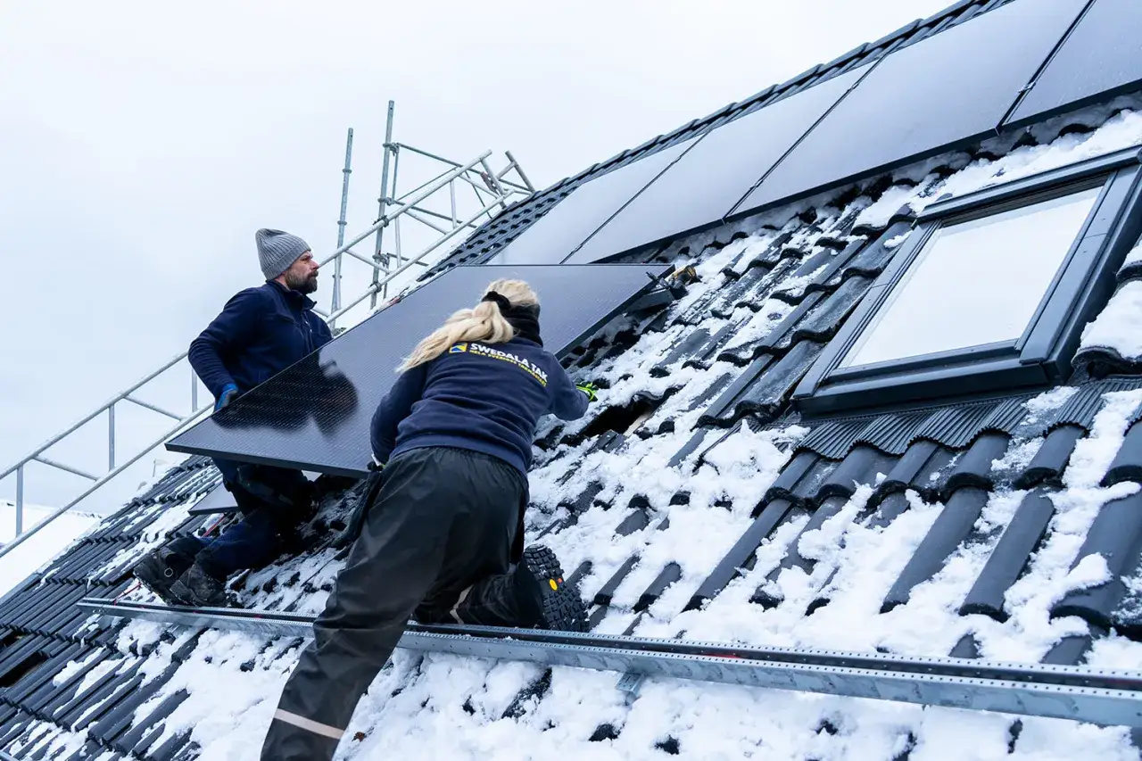 Tv&aring; personer arbetar med att installera solceller p&aring; ett sn&ouml;t&auml;ckt tak.