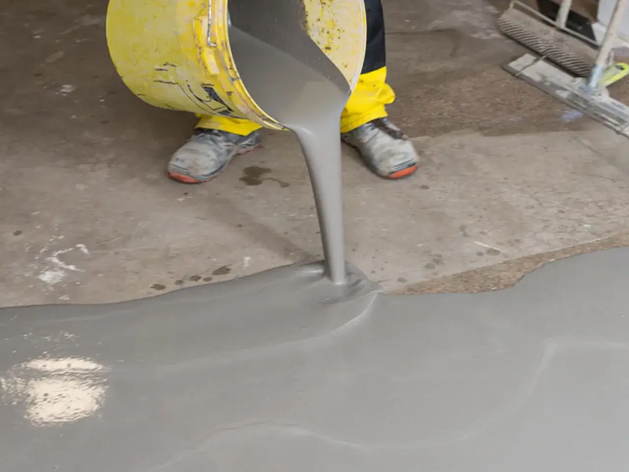 Wylewanie wylewki samopoziomującej z wiadra na betonową podłogę. Materiał tworzy gładką, jednolitą powierzchnię.