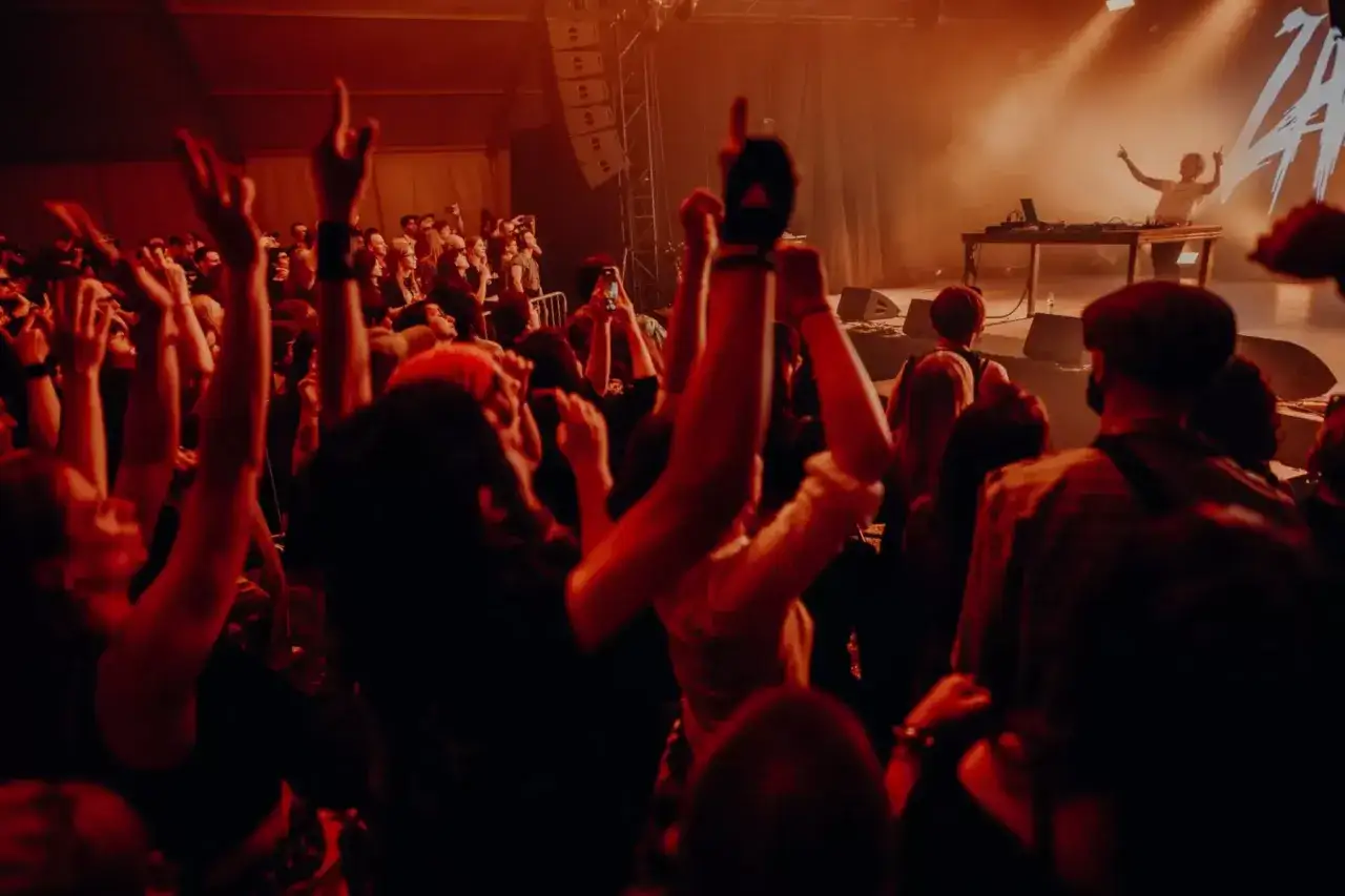 Tłum szaleje na koncercie, ręce w g&oacute;rze, światła sceny oświetlają DJ-a. Natalia Zamilska w akcji, tworzy niezapomnianą atmosferę.