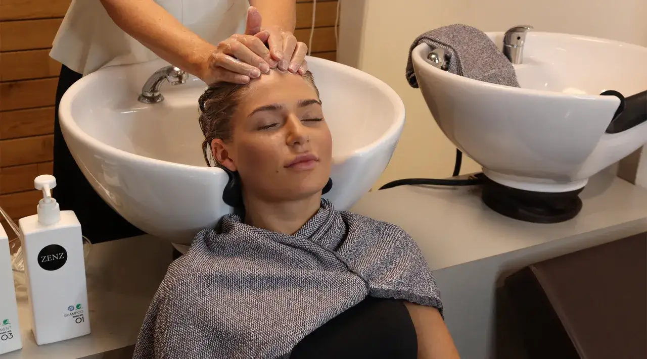 Une femme se fait laver les cheveux dans un bac de lavage. Apprenez comment faire un bon shampoing pour un moment de détente.