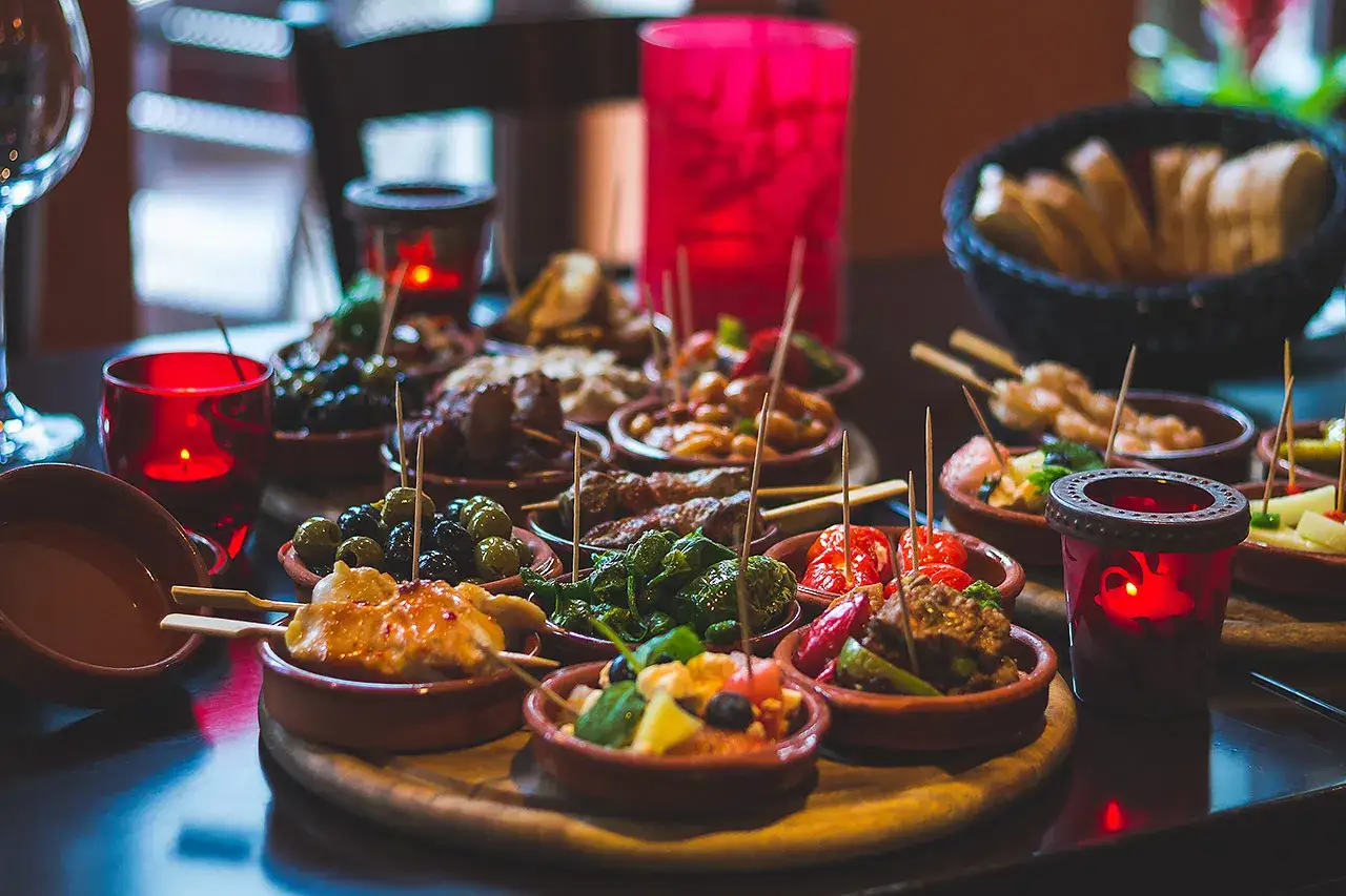 Vielfalt an kleinen Schalen mit Oliven, Fleischspie&szlig;en und Gem&uuml;se, perfekt zum **Tapas selber machen**. Rote Kerzen sorgen f&uuml;r stimmungsvolles Licht.