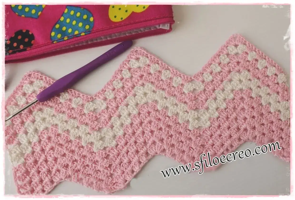 Uncinetto a punto zig zag rosa e bianco, con uncinetto viola e una pochette colorata sullo sfondo.