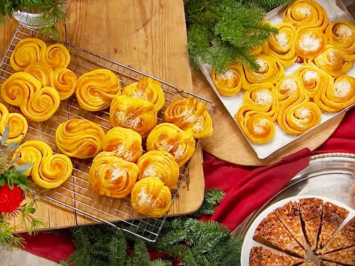 Gyllene saffransbullar med vit choklad, dekorerade med kokosflingor, ligger p&aring; ett galler och i en form. Juliga granrisgrenar ramar in bakverken.