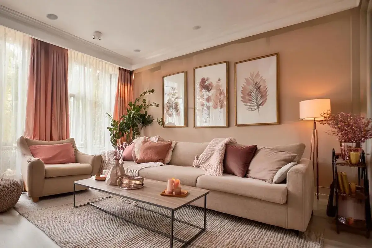 Un salon color&eacute; et chaleureux, avec un canap&eacute; beige, des coussins roses et des tableaux de feuilles.