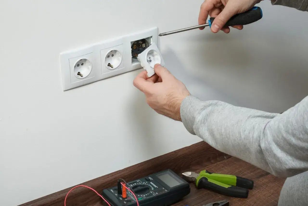 Man con destornillador y enchufe en mano, listo para cambiarlo. Herramientas el&eacute;ctricas a la vista.