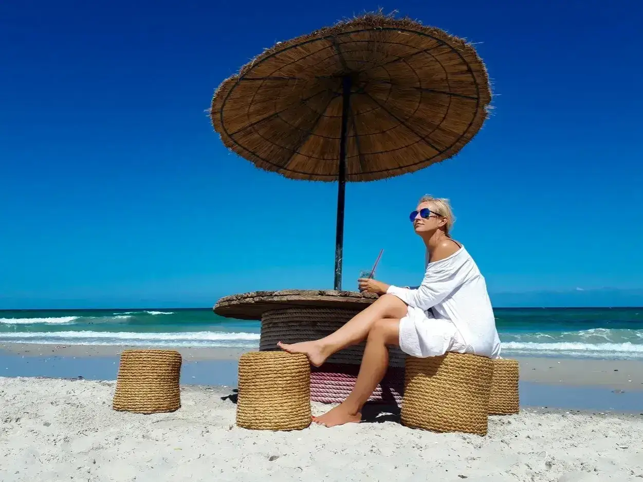 Kobieta w białej sukience relaksuje się na plaży pod parasolem. Czy Tunezja jest bezpieczna? Wygląda na to, że tak!