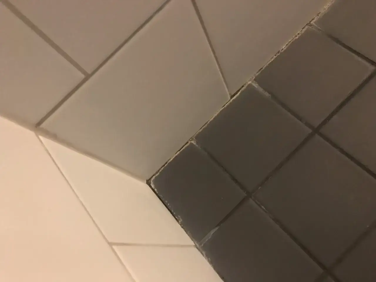 Gr&aring; och vita kakelplattor m&ouml;ts i ett h&ouml;rn. Kalkavlagringar syns l&auml;ngs fogarna, ett tydligt tecken p&aring; att det &auml;r dags att ta bort kalk.