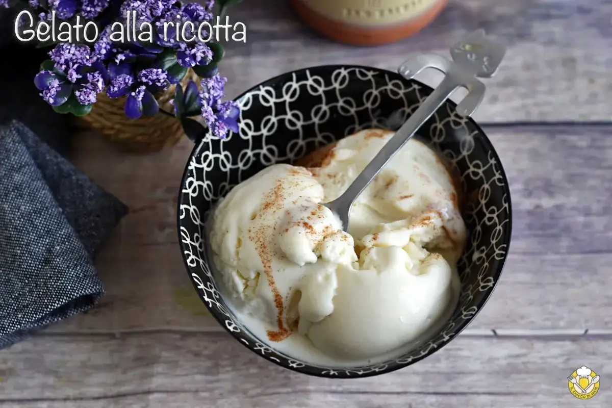 Un cremoso gelato alla ricotta, spolverato di cannella, in una ciotola decorata. Un cucchiaino a forma di gatto attende di assaggiarlo.