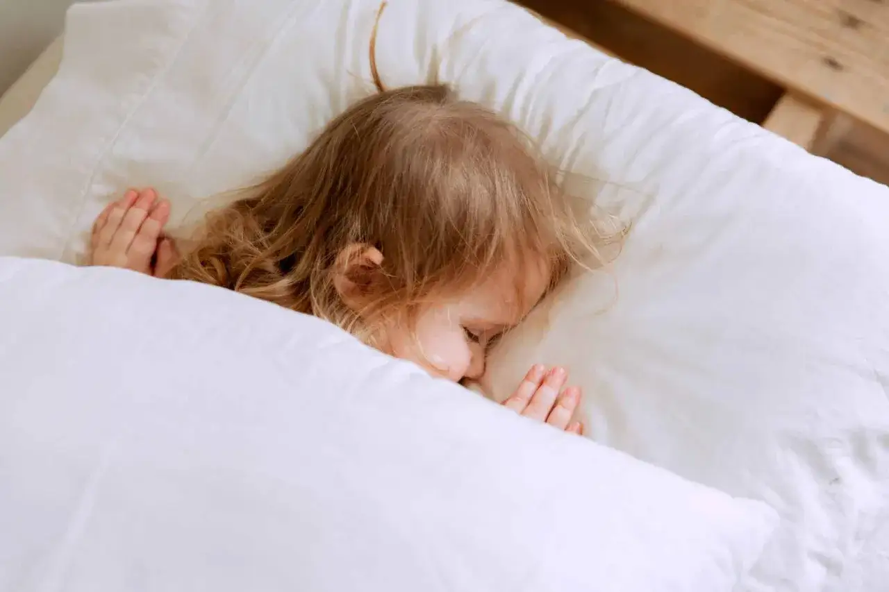 Bambina bionda dorme serena, avvolta nel lenzuolo bianco. Un momento di pace, sperando che l'enuresi notturna non disturbi il suo sonno.