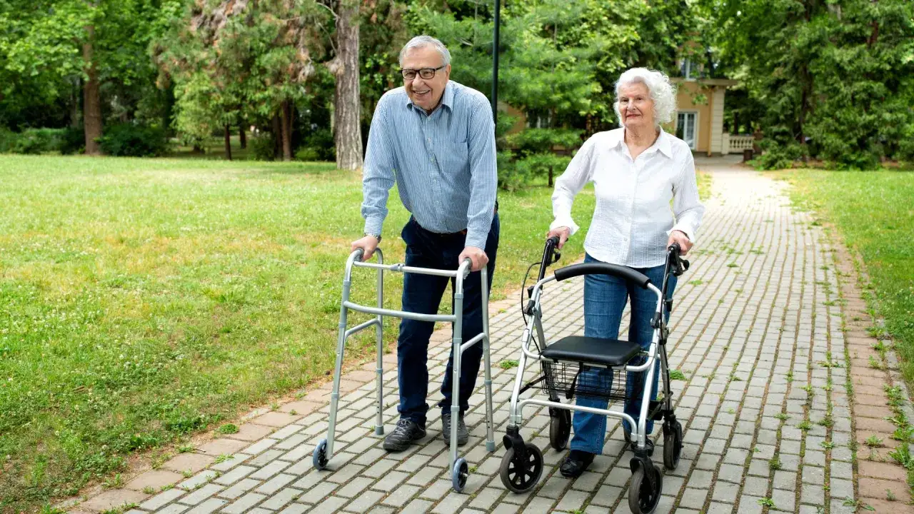Coppia anziana passeggia nel parco con deambulatore e rollator, affrontando la debolezza delle gambe cause.