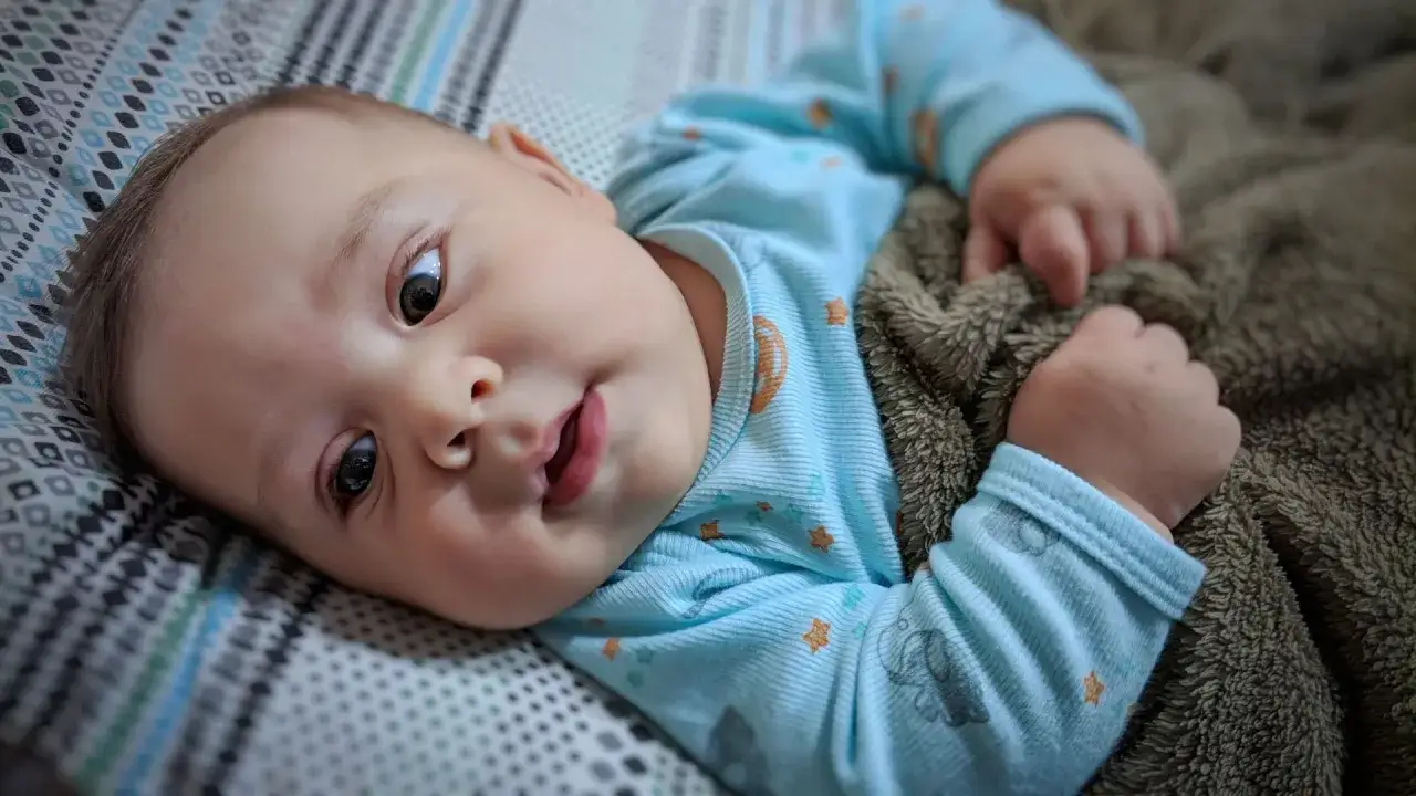 Uroczy niemowlak w niebieskim pajacyku z gwiazdkami, z zaciekawieniem patrzy na świat. Jego **sine powieki** dodają mu uroku.
