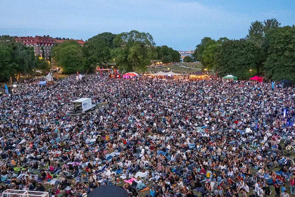 Stor publik samlad på gräsmatta för sommarbio i Stockholm. Människor sitter på filtar och njuter av kvällen.