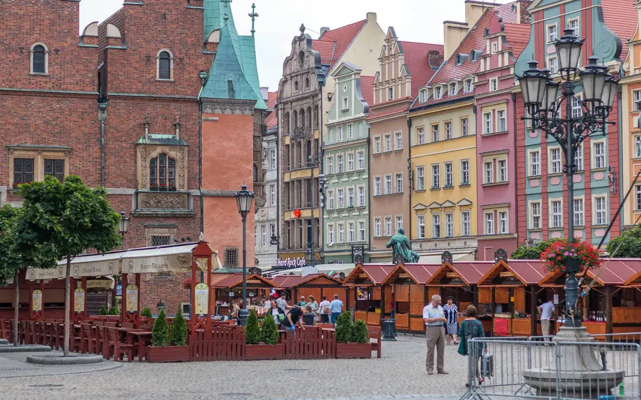 Kolorowe kamienice na starówce Wrocław ulica, z kramami i ludźmi spacerującymi po bruku.