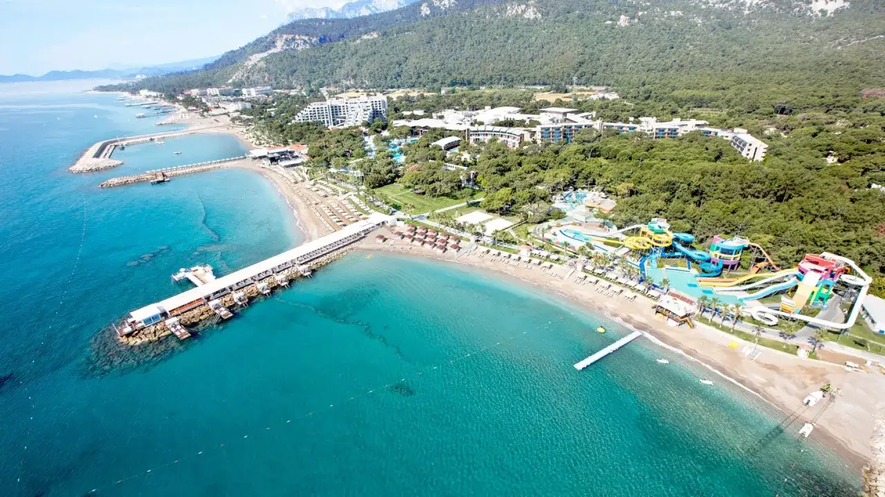 Widok z lotu ptaka na Rixos Sungate: turkusowe morze, plaża, molo, hotelowe budynki i kolorowy aquapark.