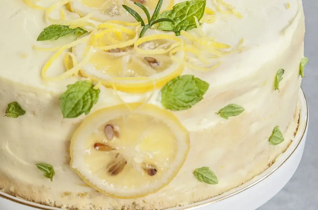 Pyszny tort cytrynowy ozdobiony plasterkami cytryny, listkami mięty i skórką cytrynową. Idealny na letnie popołudnie.