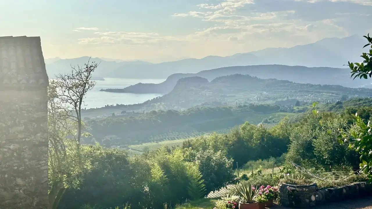 Vista panoramica di colline verdi e del lago, con montagne sfumate all'orizzonte. Un luogo incantevole dove scoprire cosa vedere ad Affi.