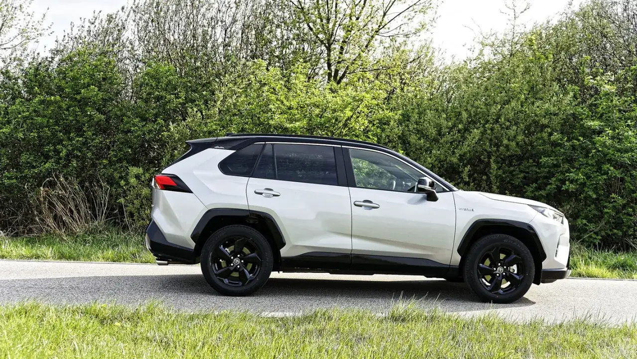 Biała Toyota RAV4 Hybrid na tle zieleni. Zastanawiasz się, ile pali Toyota RAV4? Ten model zachwyca niskim spalaniem.