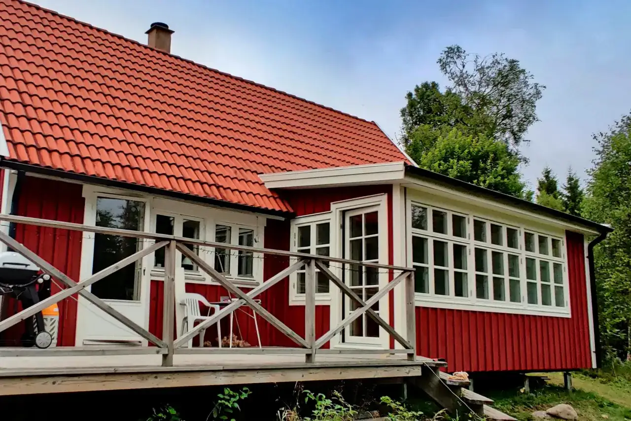 Rött hus med tegeltak och en utbyggnad av glaspartier. Trädgårdsmöbler och grill på altanen.
