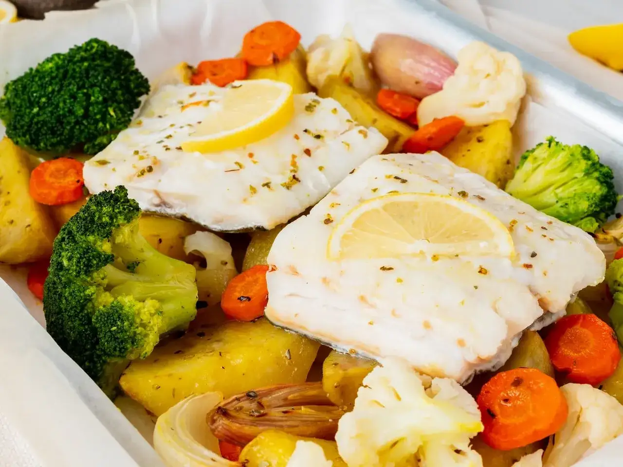 Delicioso bacalao al horno con patatas, br&oacute;coli, zanahorias y coliflor, adornado con rodajas de lim&oacute;n.