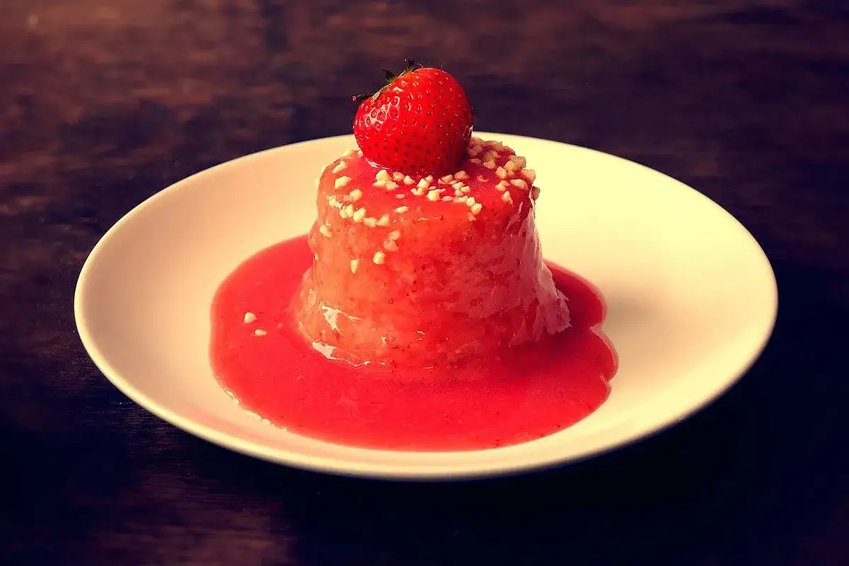 Delizioso semifreddo alle fragole, guarnito con una fragola fresca e granella croccante, servito su un piatto bianco con salsa di fragole.