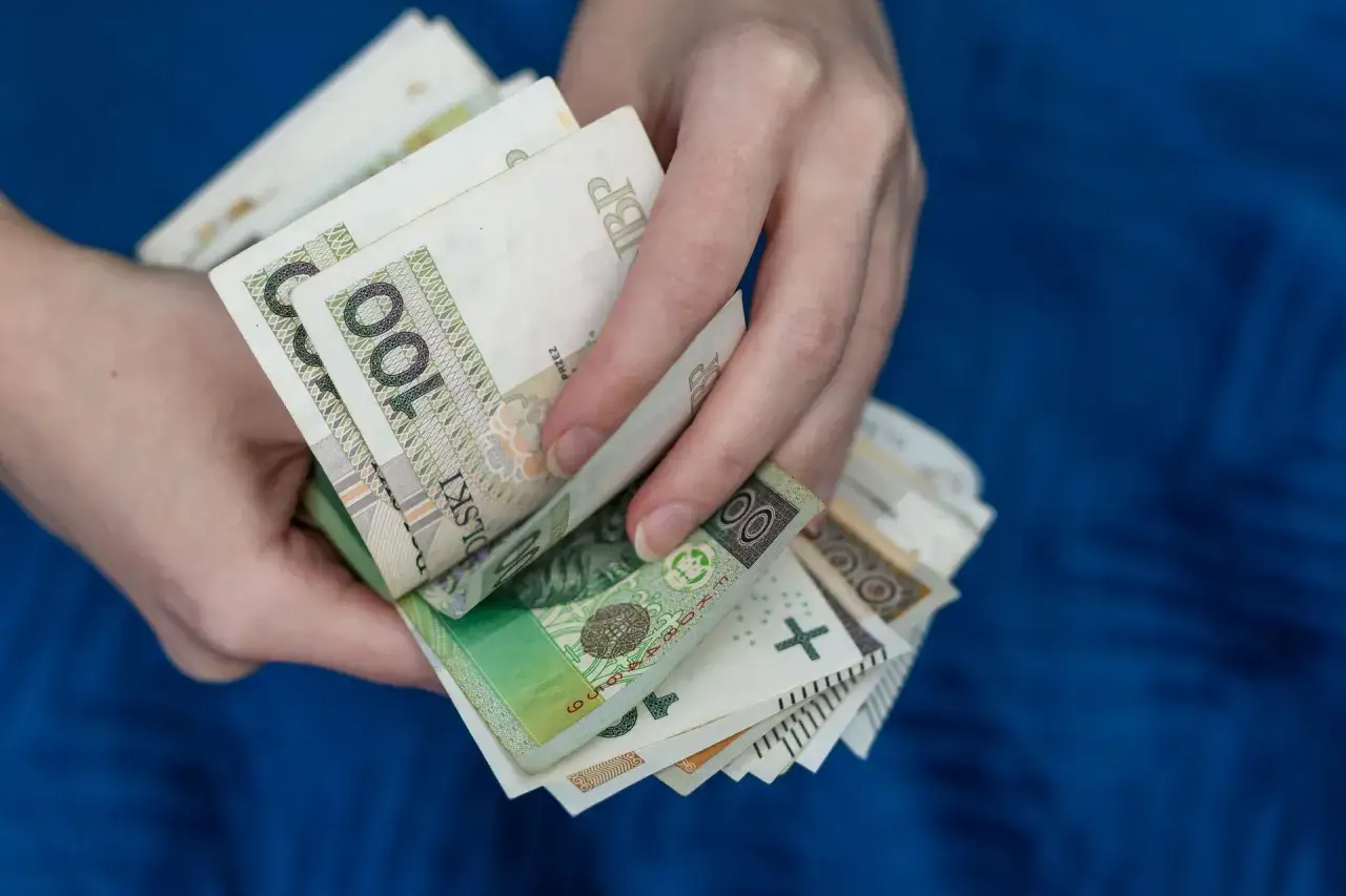 Dłonie trzymające plik banknotów 100 zł. Czy państwo może zabrać pieniądze z konta w razie wojny?