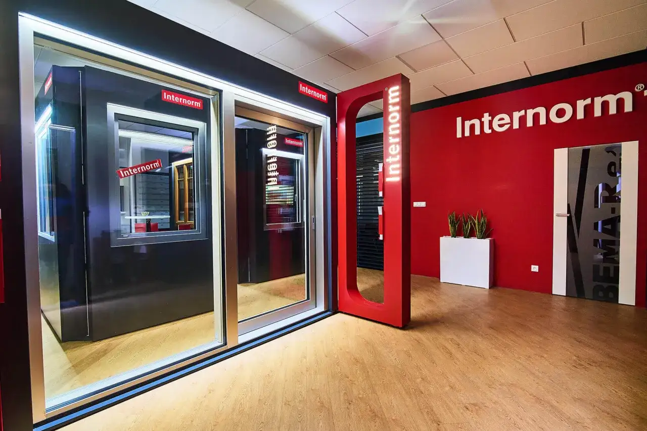 Nowoczesny salon z oknami i drzwiami Internorm, czerwone akcenty, drewniana podłoga.