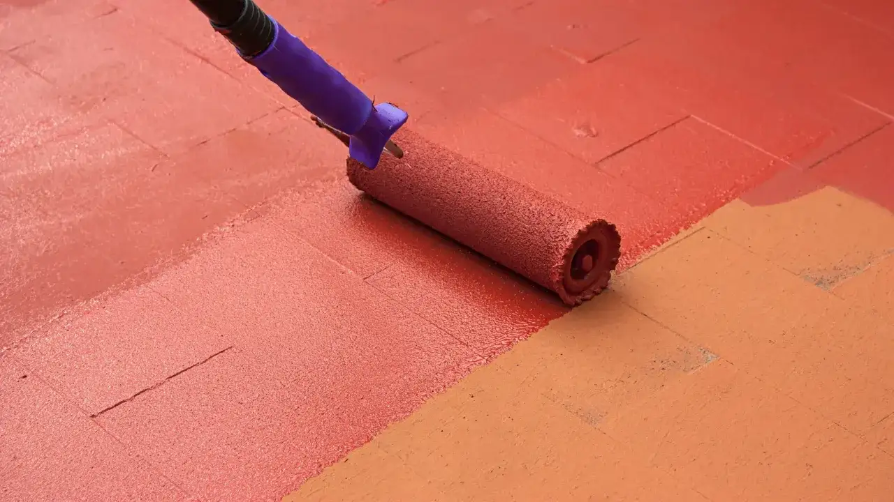Rodillo pintando el suelo de la terraza de rojo. El proceso de pintar suelo terraza est&aacute; en marcha, cubriendo las baldosas con un vibrante color.