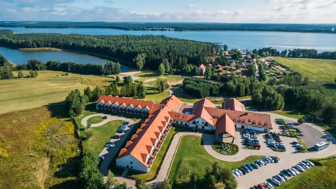 Malowniczy widok na mikołajki hotel resort spa nad jeziorem, otoczony lasem i zielenią.