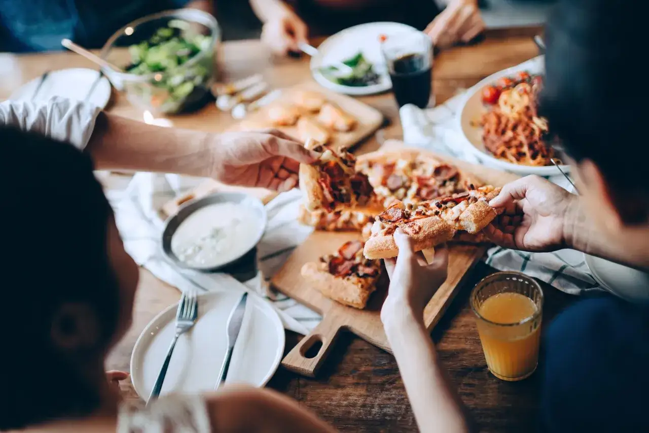 Rodzina przy stole dzieli się pizzą. Czy bon turystyczny można wykorzystać w restauracji? Tak, to świetny pomysł na rodzinny obiad!