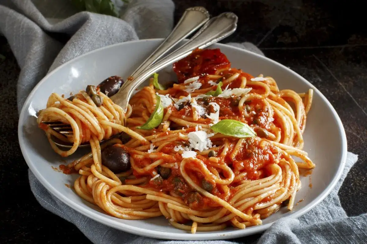Pyszne linguine a spaghetti z sosem pomidorowym, oliwkami, kaparami i bazylią, posypane parmezanem.