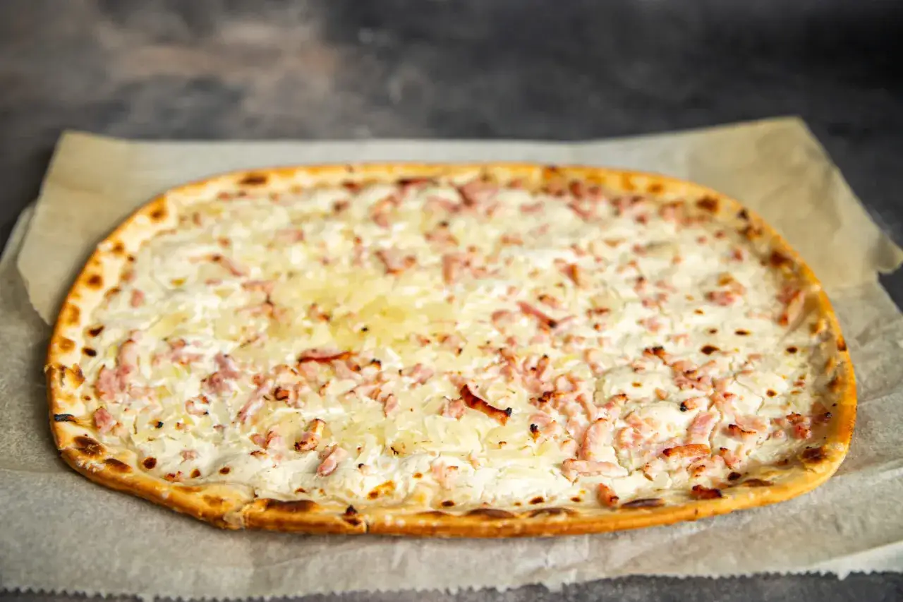 Flammekueche garnie de lardons et d'oignons, prête pour un accompagnement flammekueche parfait.
