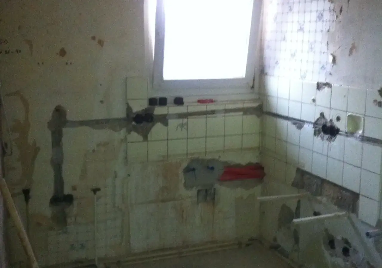 Renovierungsarbeiten: W&auml;nde mit alten Fliesen, bereit zum Verputzen. Ein Fenster erhellt den Raum.