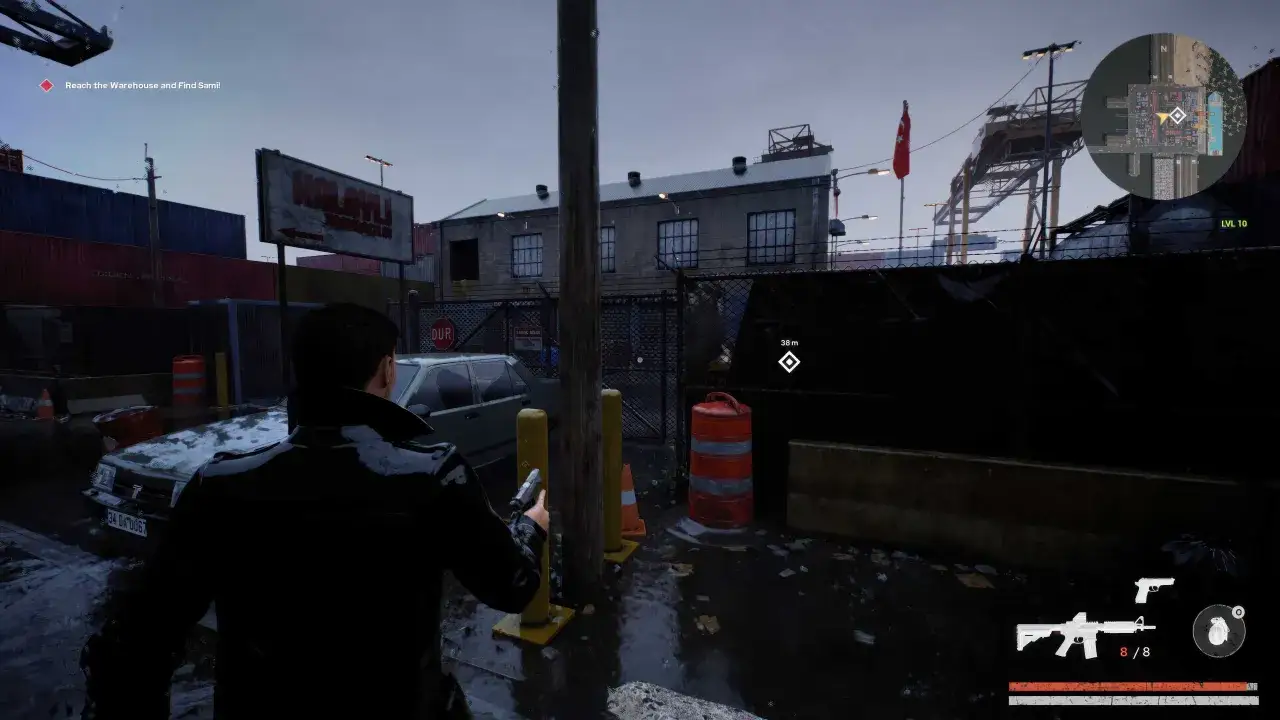 Gracz w czarnej kurtce z pistoletem w ręku, w deszczowej scenerii portu. W tle budynki i dźwigi. Gra podobna do GTA.