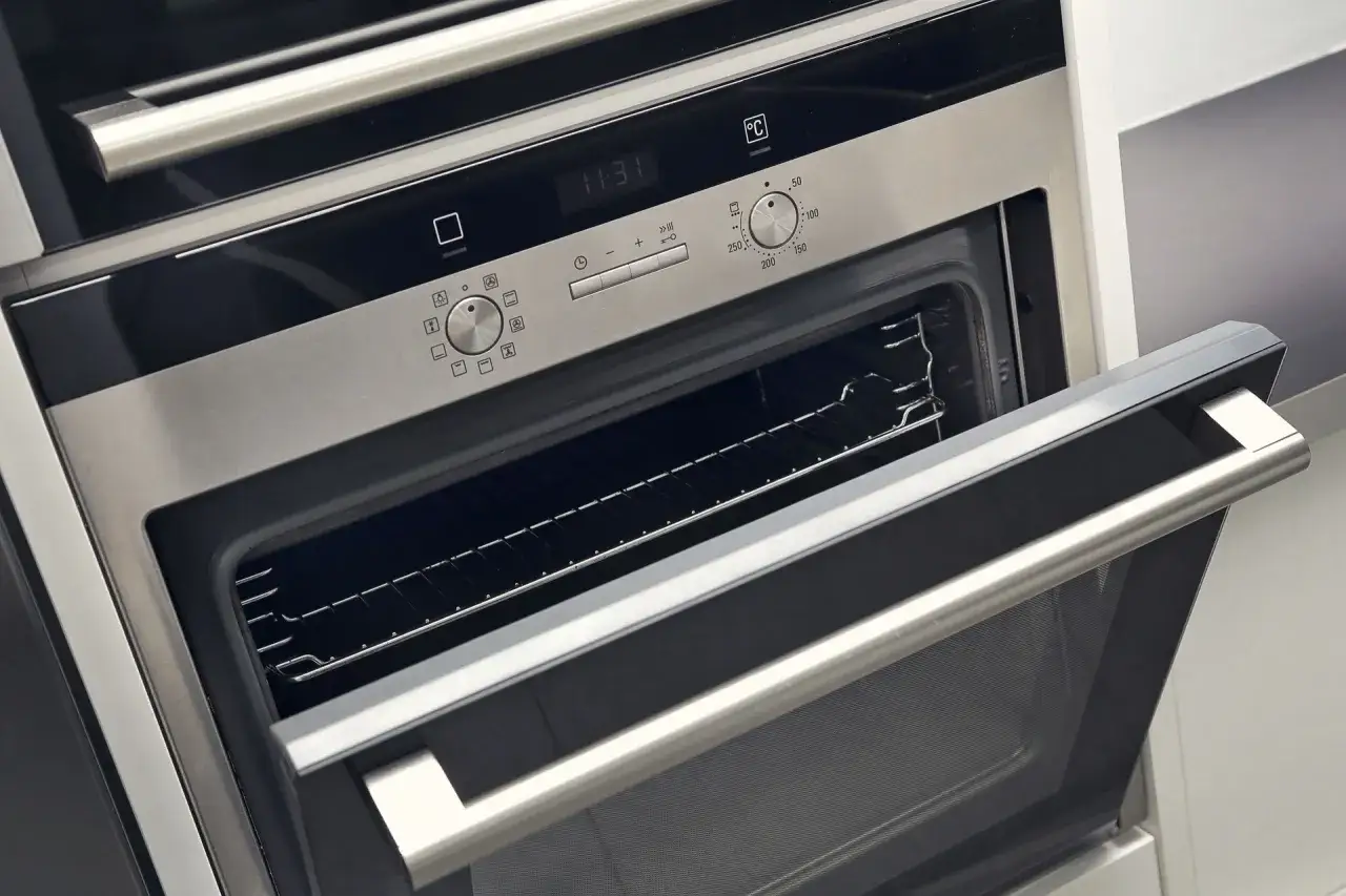 Moderner Einbaubackofen mit Edelstahldesign und ge&ouml;ffneter T&uuml;r. Ein Blick auf die Bedienelemente, die auf eine lange Lebensdauer des Backofens hindeuten.