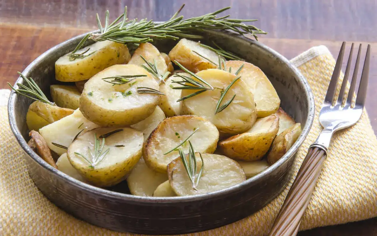 Patate novelle al forno, dorate e profumate al rosmarino, servite in una ciotola di metallo.
