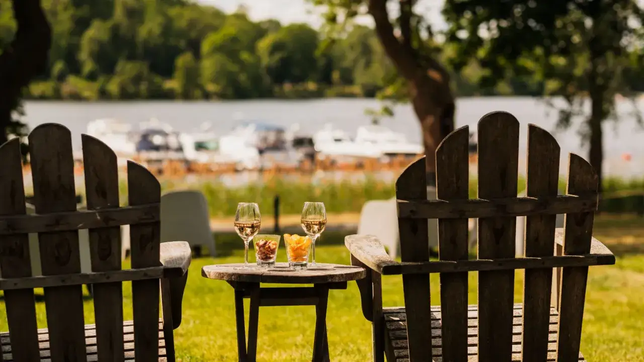 Två glas rosé och snacks på ett litet bord mellan två trästolar. En idyllisk vy över vattnet med båtar, perfekt för en avkopplande stund på Djurgården, Stockholm.