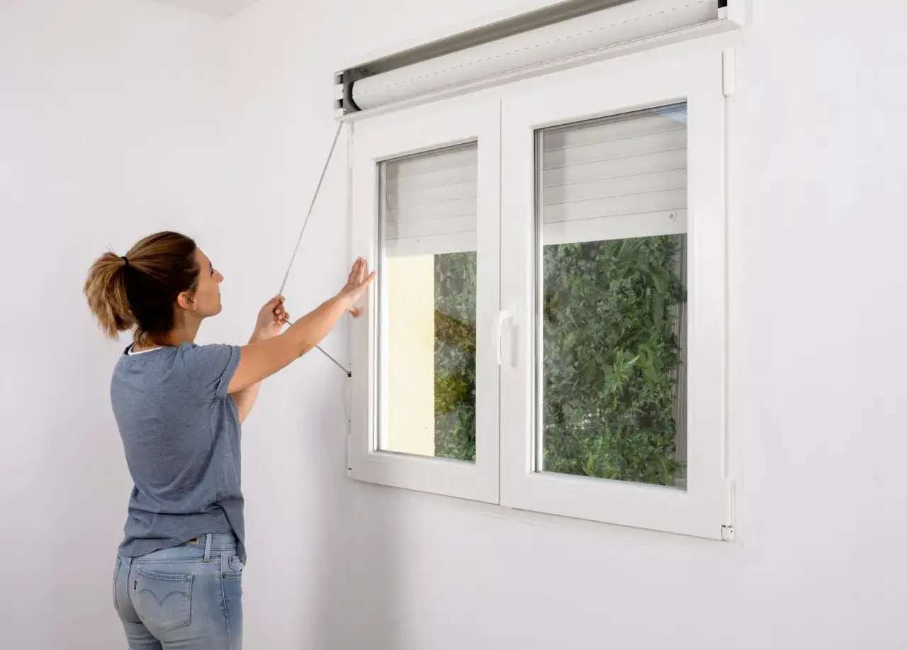Mujer realizando la instalación de persianas en una ventana blanca.